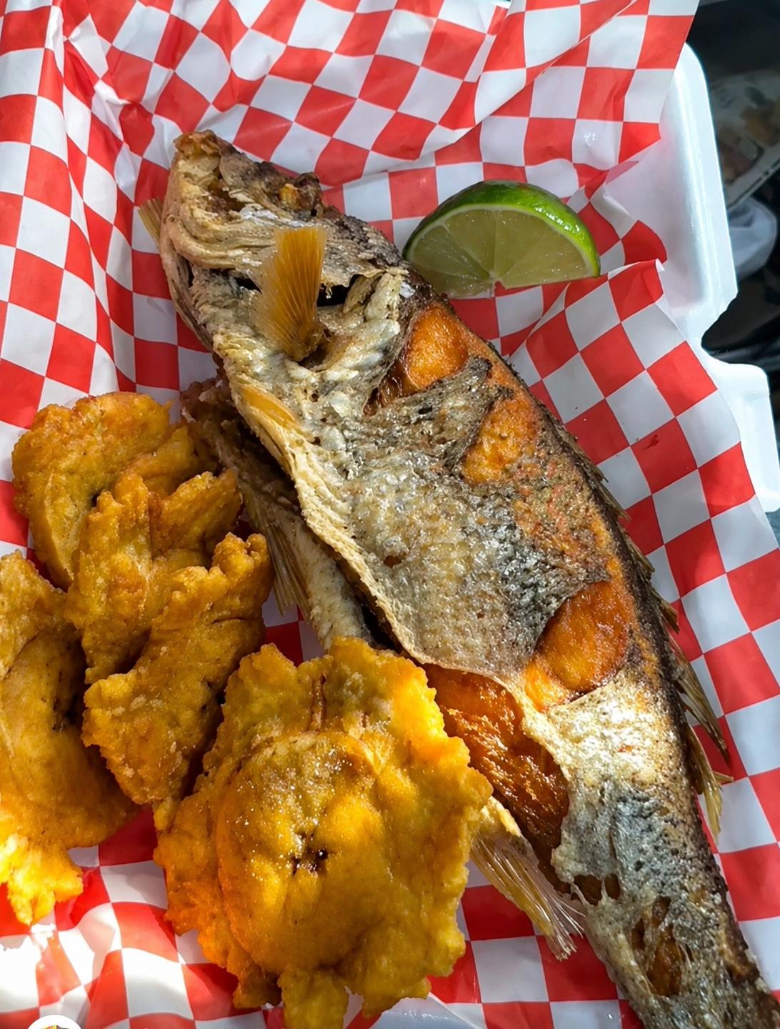 Whole fried fish with tostones and lime in a takeout container