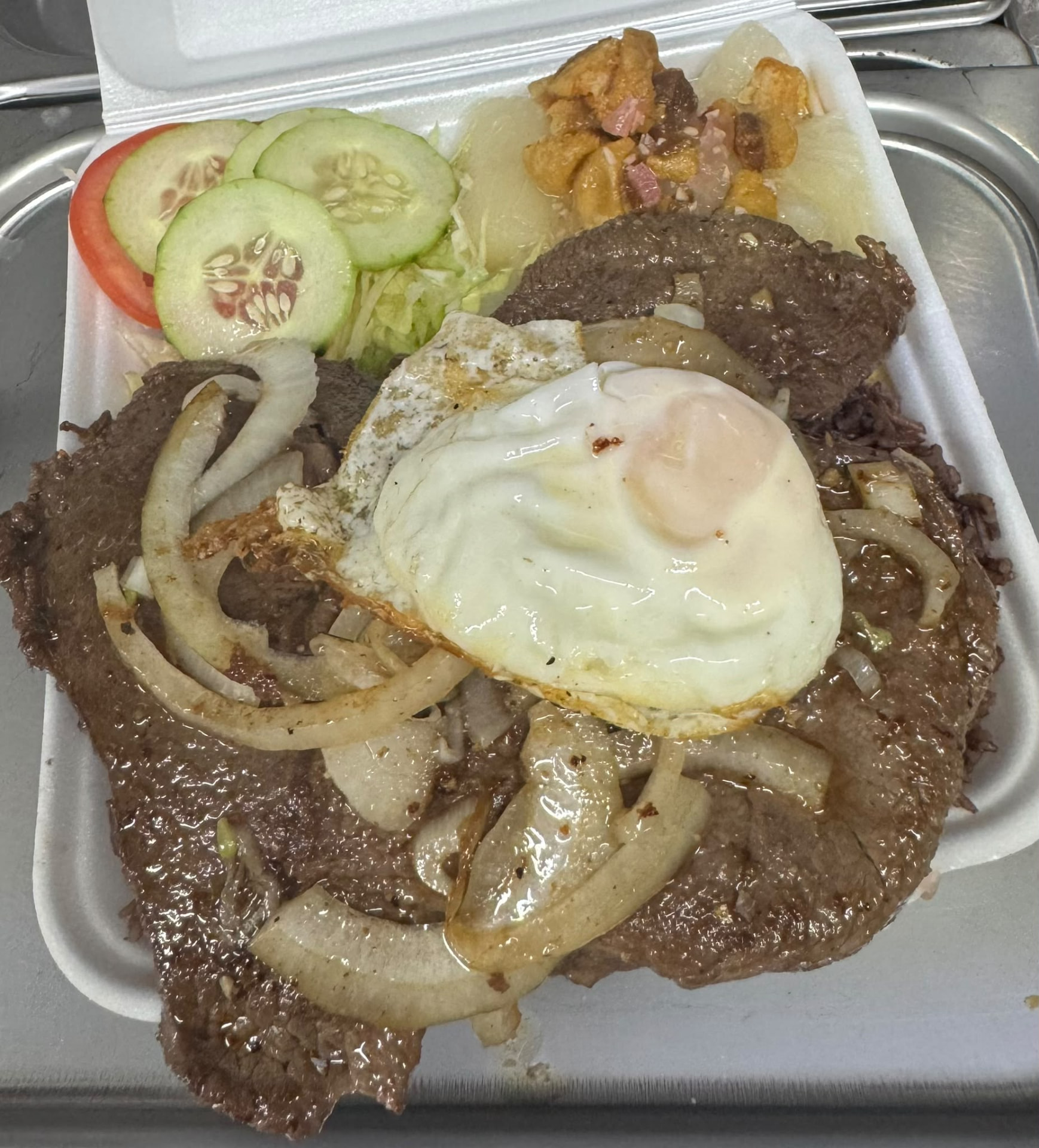 Palomilla steak topped with a fried egg, congrí rice, yuca and salad in a takeout container