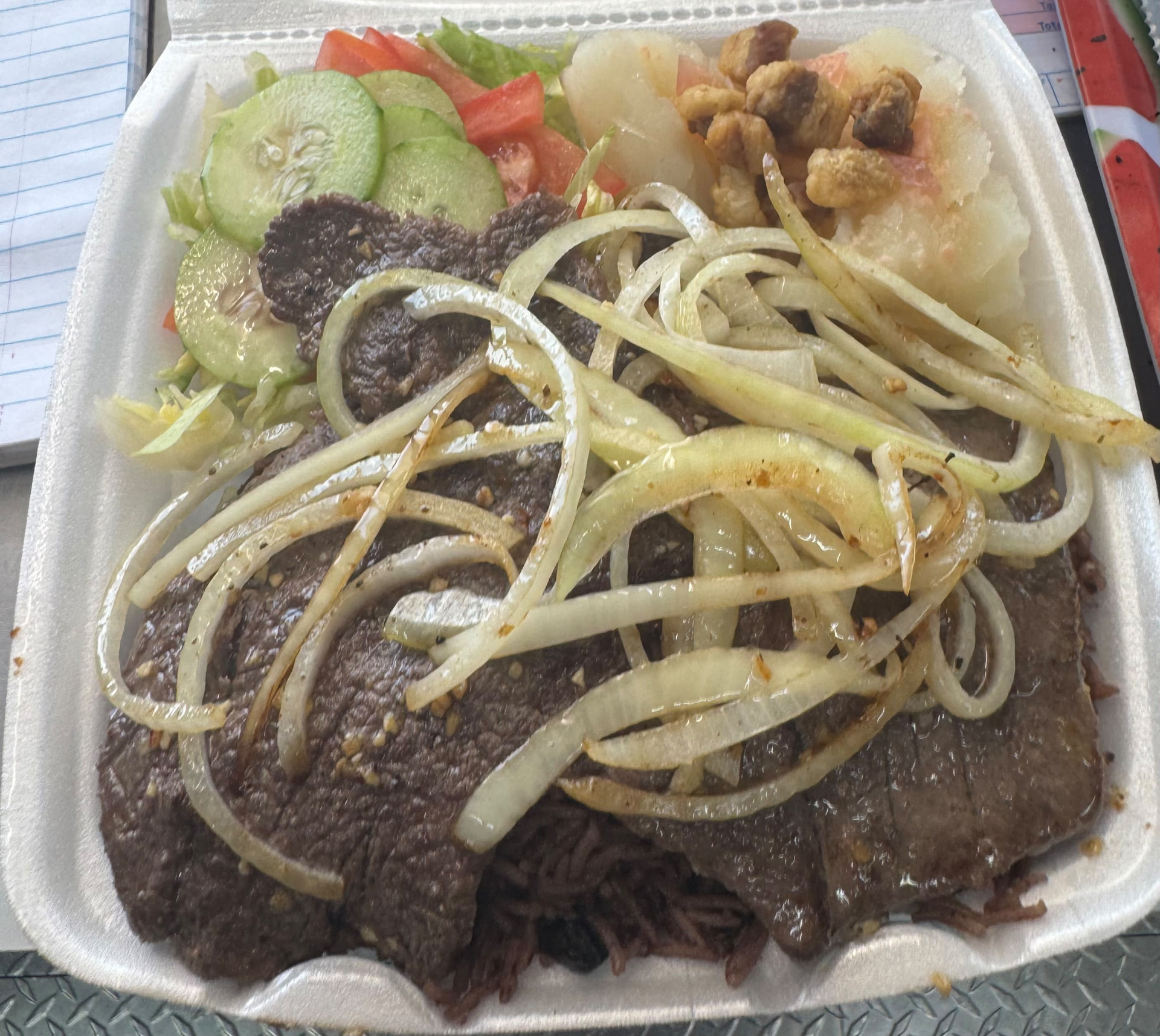 Completa de bistec de palomilla — palomilla steak with sautéed onions over congrí rice with yuca, chicharrones and salad in a takeout container