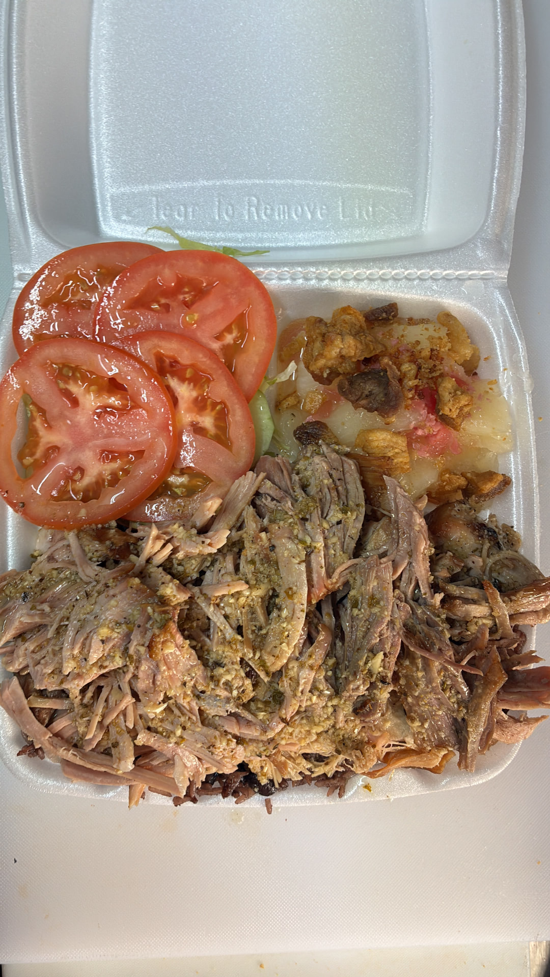 Shredded roast pork with yuca, pork cracklings, tomato and congrí rice in a takeout container