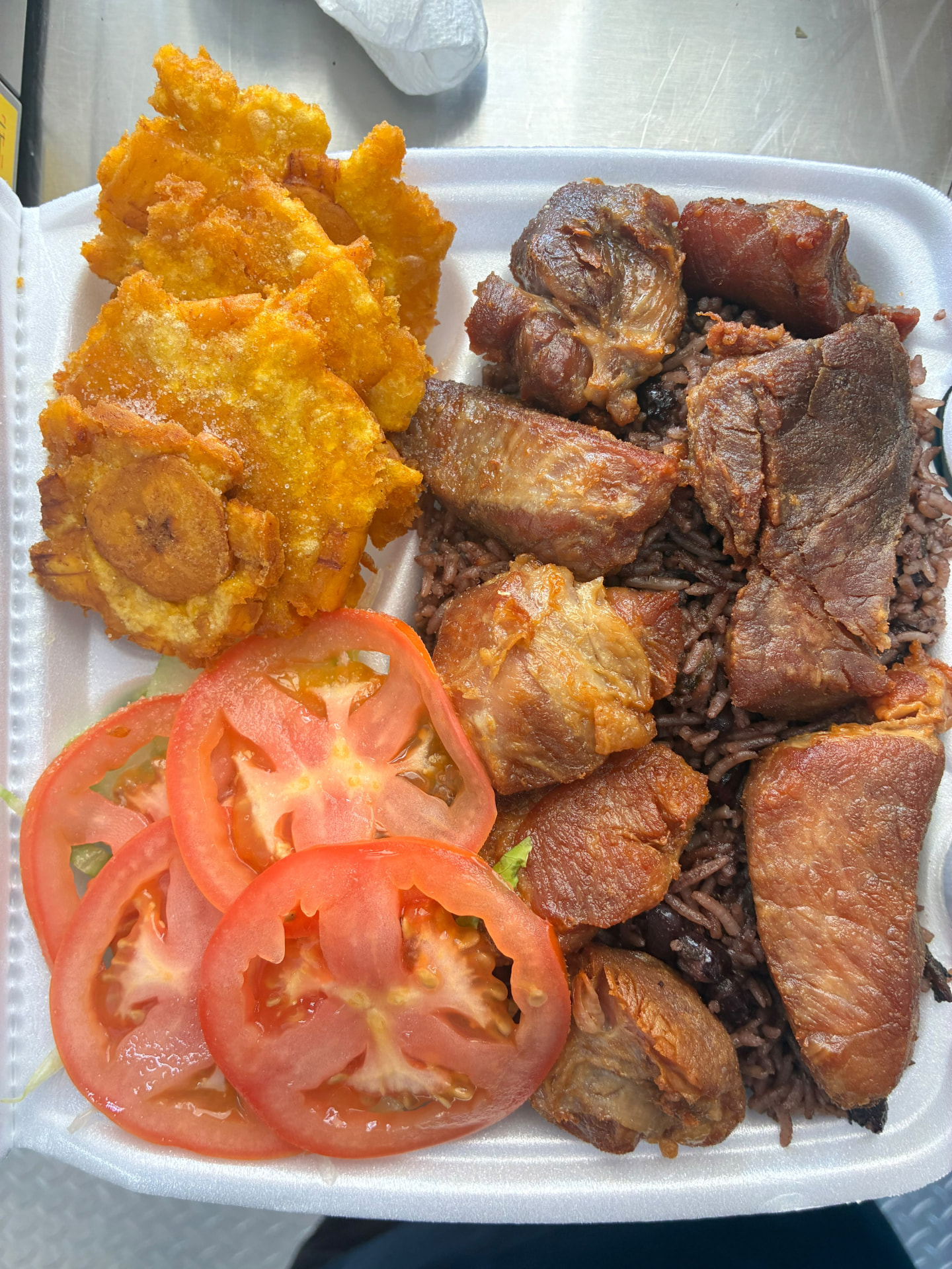 Fried pork chunks with congrí rice, tostones and tomato salad in a takeout container