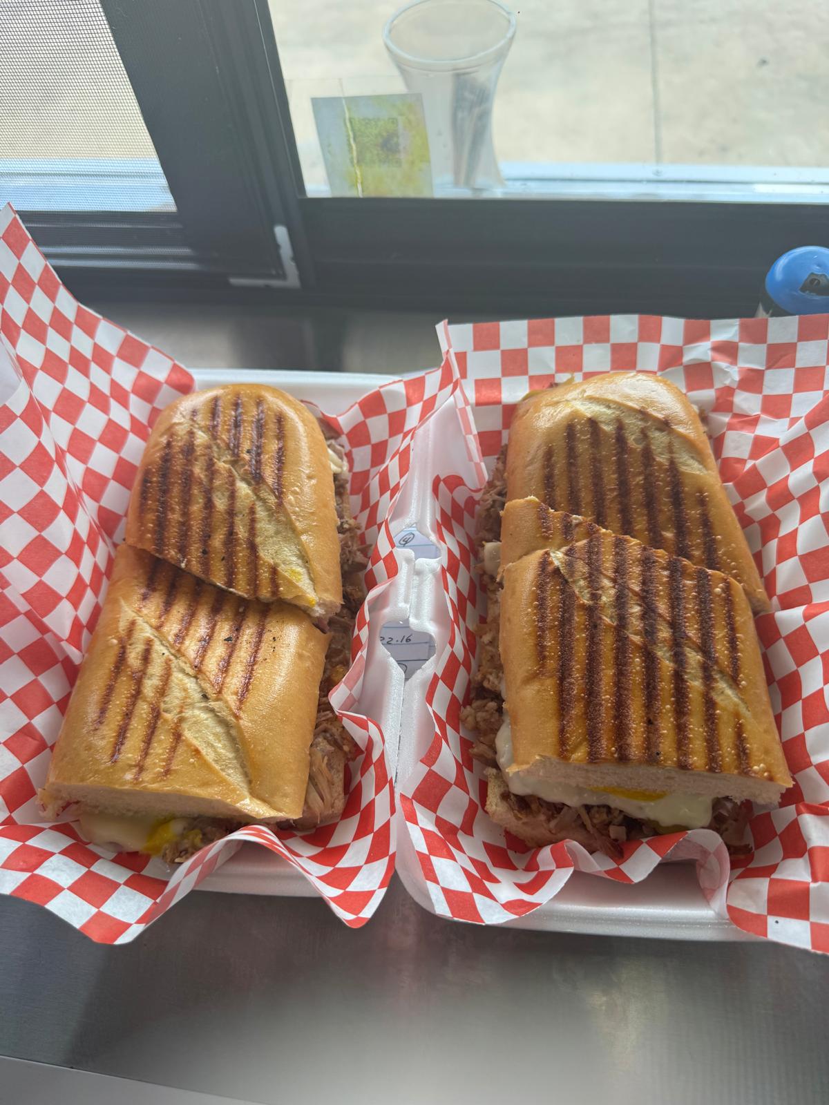 Two pressed Cuban sandwiches on red-checkered paper, fresh off the plancha