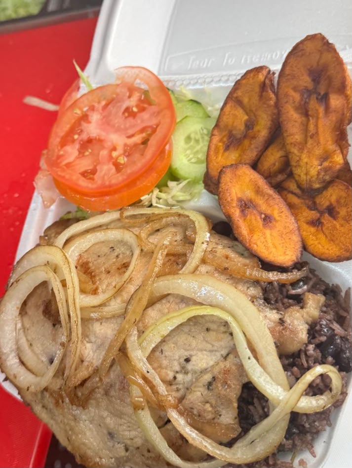 Grilled pork chops with sautéed onions, congrí rice, maduros and salad in a takeout container